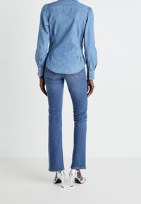 Ljusblå denimskjorta med yoke-design, långa ärmar och knappmanschetter. I kombination med mörkblå utsvängda jeans och silvriga högklackade skor.