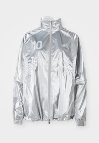 Zilveren Adidas zip-up jack met hoge kraag, elastische manchetten, "10" op de linkerborst en de tekst "TEAM GAST" over de voorkant.
