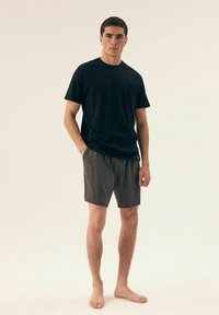 Czarna koszulka z krótkim rękawem z kieszonką na piersi, połączona z szarymi szortami. Zestaw charakteryzuje się luźnym krojem i miękkim materiałem, noszony na boso.