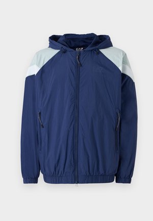 Navy windbreaker jacket with light blue accents, elastic cuffs, adjustable hood, and zippered pockets; features a textured, lightweight material.