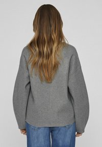 Grå, överdimensionerad tröja i ett mjukt, strukturerat tyg, med sänka axlar och rak nederkant. Matchad med medelhöga blå jeans.