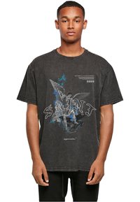 Must kolletatud T-särk mustas värvuses, millel on ingli graafiline print ja tekst "SAINT," millel on kulunud tekstuur ja kontrastsed värvid.