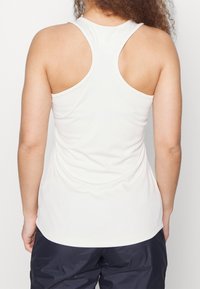 Bílý tílko s designem sportovního střihu, vyrobené z hladkého materiálu. Má přiléhavý siluetu a zakřivený lem na zadní straně.