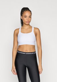 Λευκό αθλητικό μπουστάκι με φαρδιές τιράντες και λογότυπο Under Armour. Συνδυασμένο με μαύρα κολάν που έχουν ζώνη μέσης με λογότυπο. Ομαλό, ελαστικό ύφασμα.