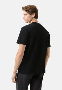 Czarny t-shirt z krótkim rękawem, o okrągłym dekolcie, gładkiej tkaninie i bocznych rozcięciach. Tył z prostym, minimalistycznym wzorem.