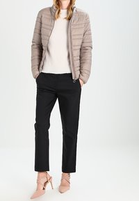 Lichtbeige pufferjack met een hoge kraag, gecombineerd met een zachte witte trui en zwarte op maat gemaakte broek. Heeft naakte hakken.