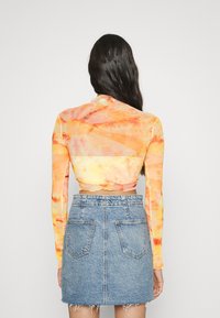 Długi rękaw, skrócona bluzka w pomarańczowym i żółtym wzorze tie-dye, w połączeniu z dżinsową mini spódnicą z dwiema tylnymi kieszeniami i postrzępionym dołem.