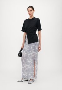 Svart knytt topp, grå tie-dye ribbet maxiskjørt med sideslit, sølvfargede flate sko, og en liten svart veske med sirkulære detaljer.
