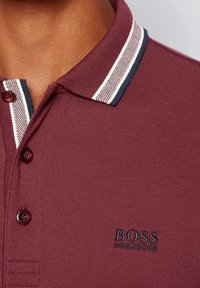 Mörkröd polo-shirt i texturerad stuv, med en klassisk krage som har marinblå och vit randig kant, samt en liten broderad "BOSS"-logotyp.