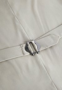 Primo piano di tessuto beige con cintura abbinata dotata di fibbia metallica argentata su un capo di abbigliamento.