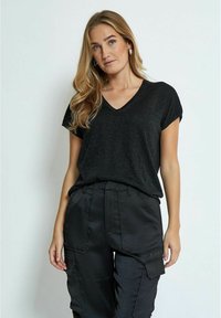 T-shirt nera con scollo a V e maniche corte, realizzata in un tessuto leggermente luccicante. Abbinata a pantaloni cargo neri con molteplici tasche.