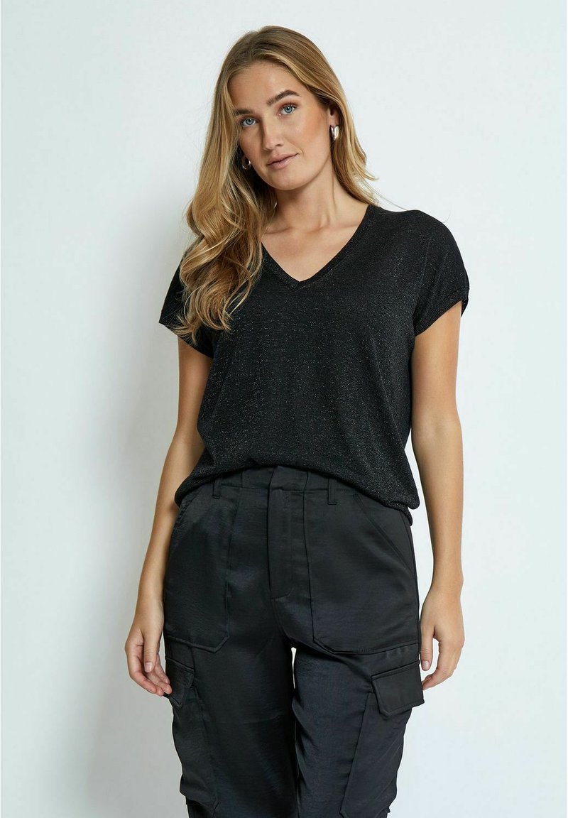T-shirt nera con scollo a V e maniche corte, realizzata in un tessuto leggermente luccicante. Abbinata a pantaloni cargo neri con molteplici tasche.