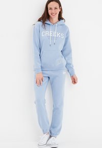 Himmelblaues Kapuzenshirt mit "CREEKS" Schriftzug, kombiniert mit passender Jogginghose. Aus einem Baumwollgemisch; verfügt über eine Fronttasche und elastische Bündchen.