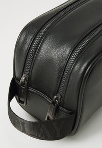 Black leather travel bag with a textured finish, dual silver zippers, and a sturdy fabric handle featuring patterned accents.