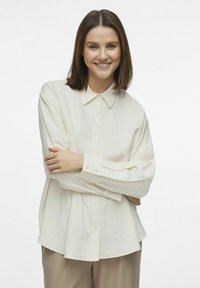 Camisa de botones color beige claro con un cuello clásico, mangas largas y un corte relajado. Fabricada con un tejido suave y ligero que tiene una textura agradable.
