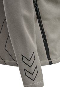 Szara teksturowana tkanina rękawa kurtki z czarnymi podwójnymi wzorami szewronowymi i czarnym pionowym zamkiem błyskawicznym po bokach.