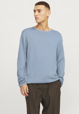 Suéter de manga larga texturizado en azul claro con cuello redondo y corte relajado, combinado con pantalones marrón oscuro. Diseño minimalista, sin patrones visibles.