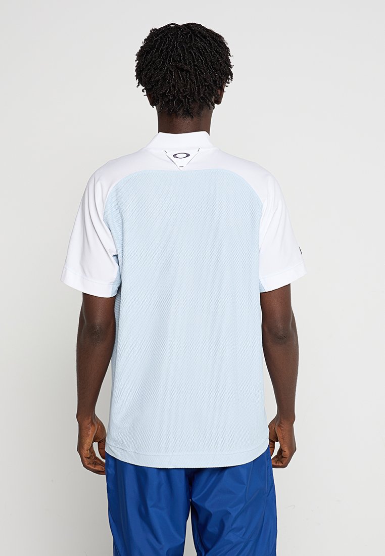 Hellblaues Sportshirt mit weißen Raglanärmeln, strukturiertem Rücken und Logo am Kragen, kombiniert mit blauen Shorts.