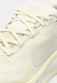 Scarpa sportiva gialla chiaro con tomaia testurizzata, dettagli lisci, logo Nike ben visibile e lacci sovrapposti per una vestibilità sicura.