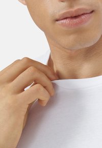 Weißes Baumwoll-T-Shirt mit Rundhalsausschnitt, leicht von einer Hand gehalten. Der Hautton ist sichtbar, mit glatter Textur und dezenten Gesichtszügen.