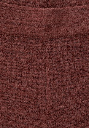 Nahaufnahme eines strukturierten, gerippten Stoffes in dunkelrotbrauner Farbe mit sichtbaren Nähten, die ein dezentes V-förmiges Muster bilden.