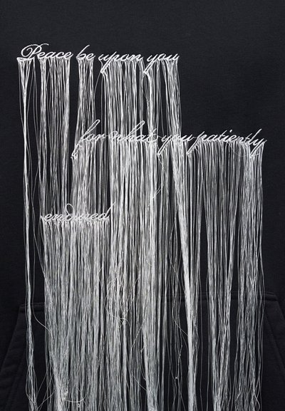 Bel vezen tekst z dolgimi ohlapnimi nitmi na črni tkanini pravi: "Mir naj bo z vami, bodite popolni in potrpežljivi."