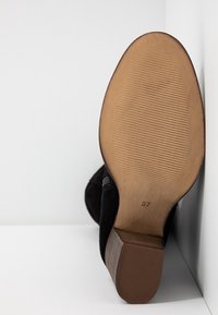 Semelle d'une botte noire avec un petit talon en bois, semelle texturée et taille 37 visible sur fond blanc.