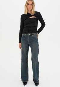 Zwarte lange mouwen top met een gedraaide ontwerp en uitsnijding, gecombineerd met hoge taille blauwe recht-pijpen jeans en puntige zwarte hakken.
