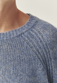 Pull en maille bleu avec un motif texturé, doté d'un col rond côtelé et de manches raglan. Tissu doux et léger avec une légère brillance.