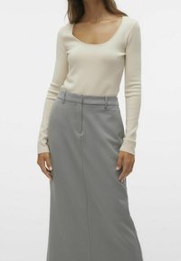 Krämfärgad långärmad topp med rundad halsringning, kombinerad med en högmidjad grå kjol med slät textur och skräddarsydd design.