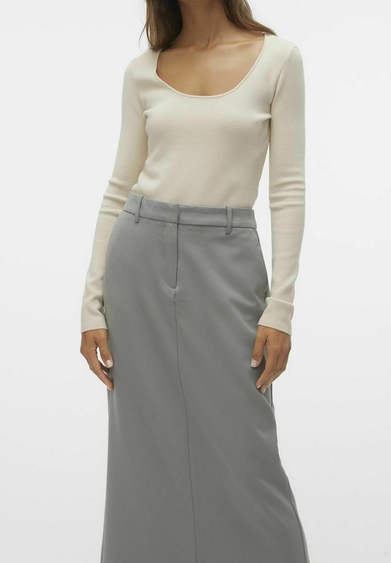 Krämfärgad långärmad topp med rundad halsringning, kombinerad med en högmidjad grå kjol med slät textur och skräddarsydd design.