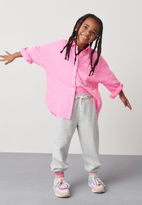 Pink button-up shirt, gray sweatpants, and multicolored sneakers. The shirt has a pocket; the pants are cuffed at the ankles.