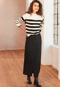 Suéter a rayas en crema y negro, combinado con una falda larga negra, que tiene una abertura frontal. Botines negros completan el atuendo.