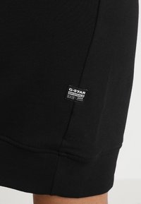 Gros plan d'un short en tissu noir avec une petite étiquette logo G-Star Originals Raw denim noir et blanc près de l'ourlet.