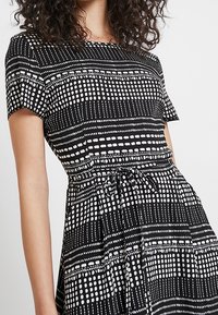 Svart och vit mönstrad klänning med korta ärmar, med ränder och prickiga mönster, en åtsittande midja och en knytning för justering.