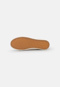Suola di scarpa in gomma con un motivo a nido d'ape, caratterizzata da un bordo esterno bianco e una soletta interna beige. Texture liscia, progettata per offrirti aderenza e durabilità.