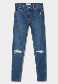 Vaqueros pitillo de mezclilla azul oscuro con cintura de altura media, que presentan parches desgastados en ambas rodillas y diseño clásico de cinco bolsillos con costuras doradas.