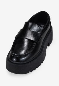 Mocassini neri in ecopelle con suola platform spessa, punta tondeggiante e una fascia larga sulla parte superiore. Finitura testurizzata e dettagli cuciti.