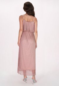 Rochie maxi din material roz deschis strălucitor, cu bretele subțiri, design în straturi și o siluetă fluidă. Pantofi cu toc înalt argintii vizibili.