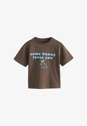 Braunes T-Shirt mit kurzen Ärmeln und hellblauem Text "some bunny loves you" sowie einer einfachen blauen Kaninchenillustration unter dem Text.