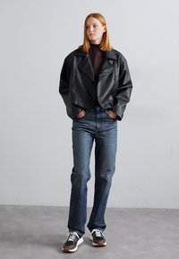 Veste en cuir noir courte, haut à col montant, jeans en denim bleu et baskets sombres. Texture lisse, large col, coupe décontractée.