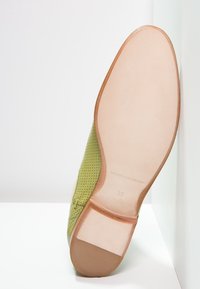Zapato de cuero perforado verde con suela beige. Presenta una punta redondeada, un diseño minimalista y una marca en la plantilla. Talla 39.