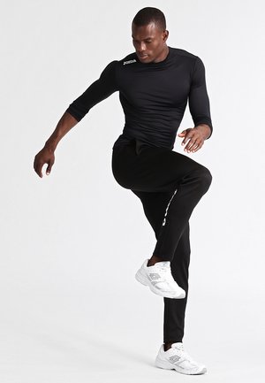 Black long-sleeve athletic shirt with a fitted design and white logo, paired with black tapered pants and white sneakers.