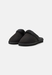 Sorte slip-on tøfler med en myk, lodden overdel og en flat, teksturert gummisåle. Designet er glatt med en avrundet tå og ingen synlig maskinvare.