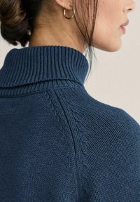 Pehmeä neulepusero tummansinisenä, jossa on poolokaulus. Ominaisuuksiin kuuluu resorikaulus ja hienovarainen pinta, jossa koristeellinen sauma olkapään kohdalla.