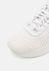 Biały pleciony sneaker z teksturowaną cholewką z tkaniny, elastyczną konstrukcją, białą gumową podeszwą i białymi sznurówkami. Minimalistyczne detale designu.