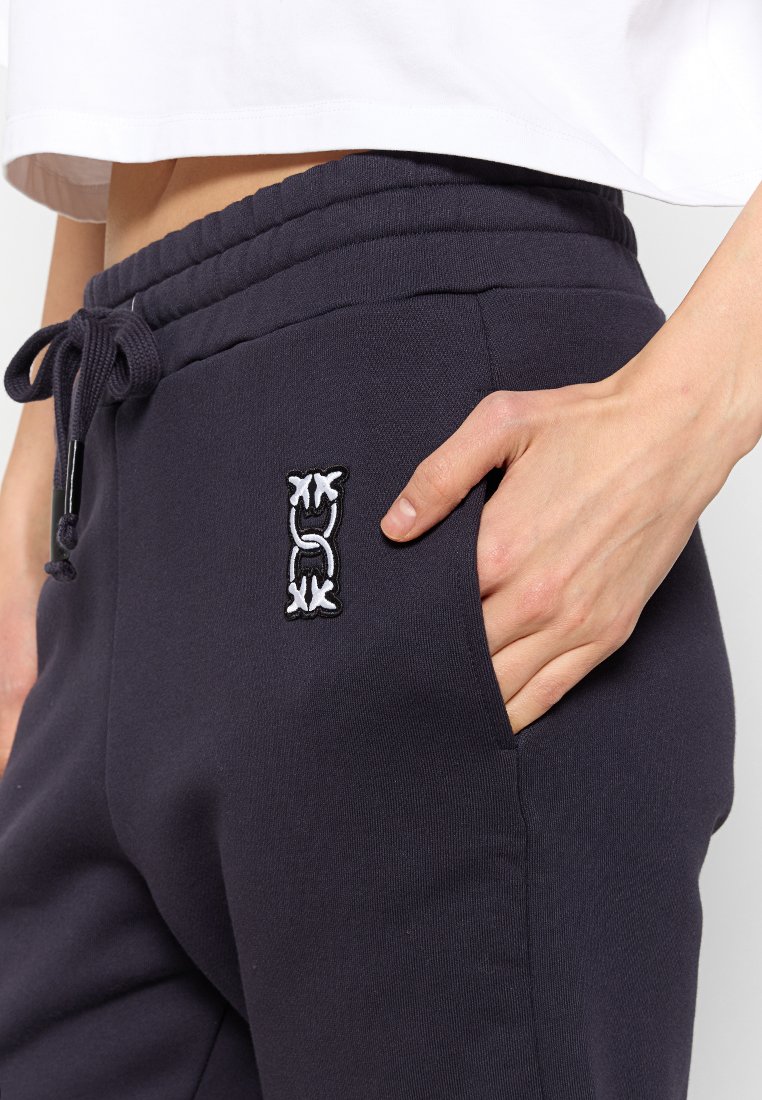 Granatowe spodnie dresowe z elastycznym paskiem w talii, sznurkiem, boczną kieszenią i białym haftowanym logo na udzie. Miękka bawełniana tkanina.
