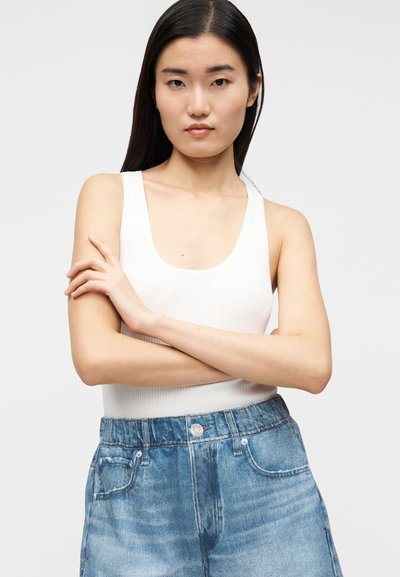 Débardeur blanc côtelé à larges bretelles, associé à un short en denim bleu clair avec une coupe décontractée et un design traditionnel à cinq poches.