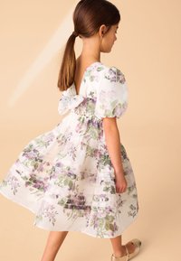 Bela obleka s purpurnim cvetličnim vzorcem, puff rokavi, nabranim pasom in detajlom s pentljo na hrbtni strani. Prosojne plasti tkanine ustvarjajo mehko teksturo.