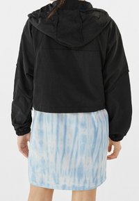 Czarna krojona kurtka z kapturem, z elastycznymi mankietami. Nosi się ją na niebieskiej spódnicy z efektem tie-dye z pionowymi wzorami. Gładka tekstura na całej powierzchni.